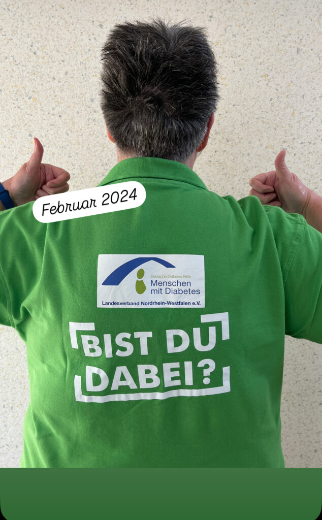 Bildbeschreibung: Rückenansicht von mir. Ich trage ein grünes T-Shirt der DDH-M NRW e.V.  mit dem Aufdruck Bist Du dabei?